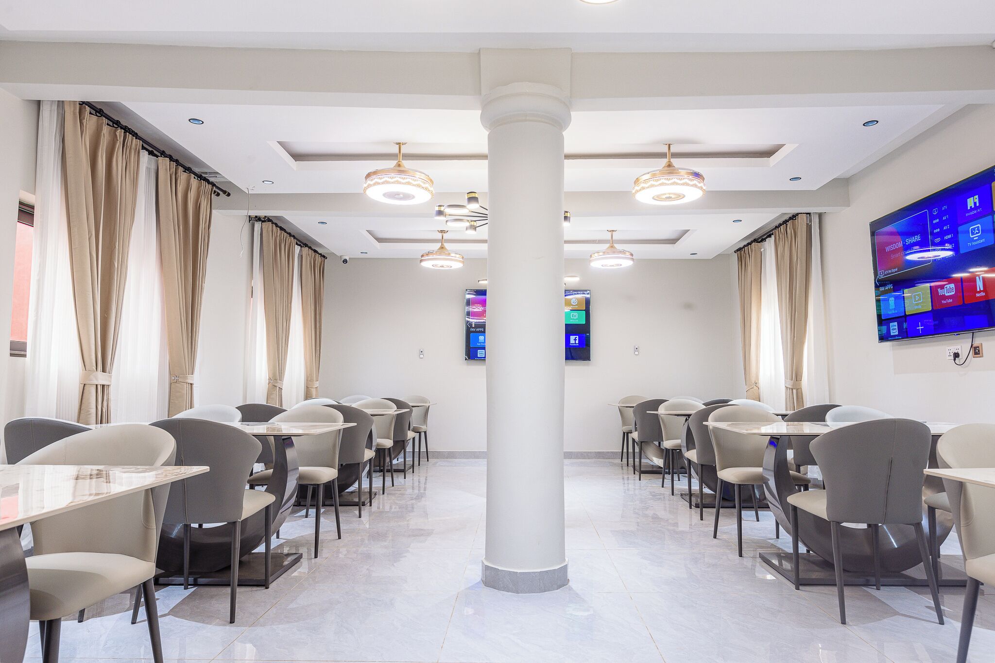 A modern dining area with tables and chairs, a large pillar, recessed lighting, and a digital screen on the wall.