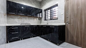 A kitchen with black marble cabinets, a wooden door, and a window with bars. - Capital 11 Hotel (North Legon)
