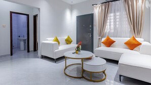 A modern living room with a white sofa set, a round coffee table, and a door leading to a bathroom. - Capital 11 Hotel (North Legon)