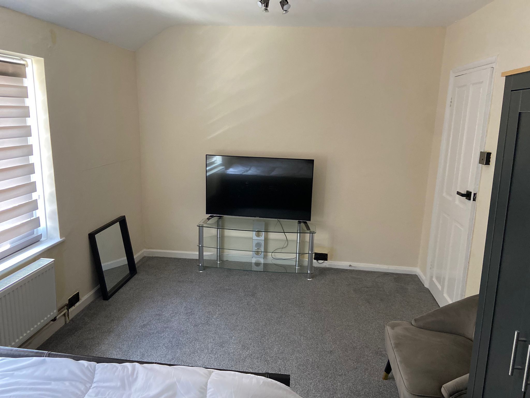 A bedroom with a television on a glass stand, a bed, a door, and a radiator.