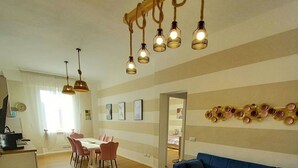 A spacious living area with a blue sofa, wooden flooring, a dining table with chairs, and a kitchen area in the background. - Third floor (Pisa)