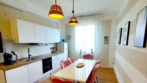 A compact kitchen with white cabinets, a microwave, and a sink. There is a dining table with six chairs and two hanging pendant lights. - Third floor (Pisa)