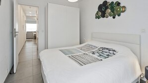 A bedroom with a bed, a white wardrobe, a wall-mounted light fixture, and a decorative wall piece. - Apartment in Blankenberge With Sea Views (Blankenberge)