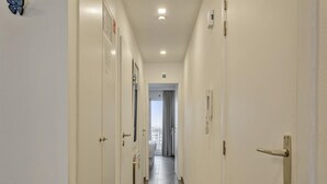 A hotel corridor with white doors, a phone on the wall, and a view of a balcony with curtains. - Apartment in Blankenberge With Sea Views (Blankenberge)
