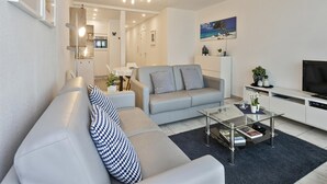 A modern living room with a grey sofa, a glass coffee table, and a flat-screen TV. - Apartment in Blankenberge With Sea Views (Blankenberge)