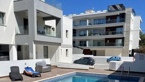A modern building with a swimming pool, outdoor seating, and a car parked nearby. - Luxury 3 Bedroom Penthouse apartment with sea view.
10 mins walk to Venus Beach (Paphos)