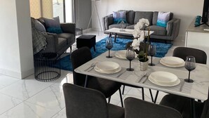 A modern dining area with a marble floor, a dining table set for four, and a grey sofa in the background. - Luxury 3 Bedroom Penthouse apartment with sea view.
10 mins walk to Venus Beach (Paphos)