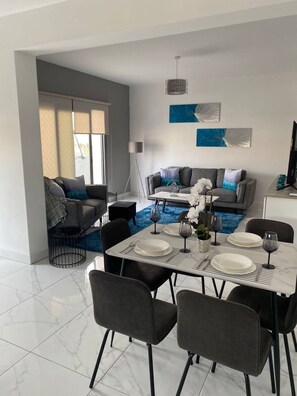 Ein moderner Essbereich mit Marmorboden, einem Esstisch für vier Personen und einem grauen Sofa im Hintergrund.