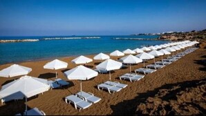 A beach with rows of white umbrellas and sun loungers facing the sea. - Luxury 3 Bedroom Penthouse apartment with sea view.
10 mins walk to Venus Beach (Paphos)