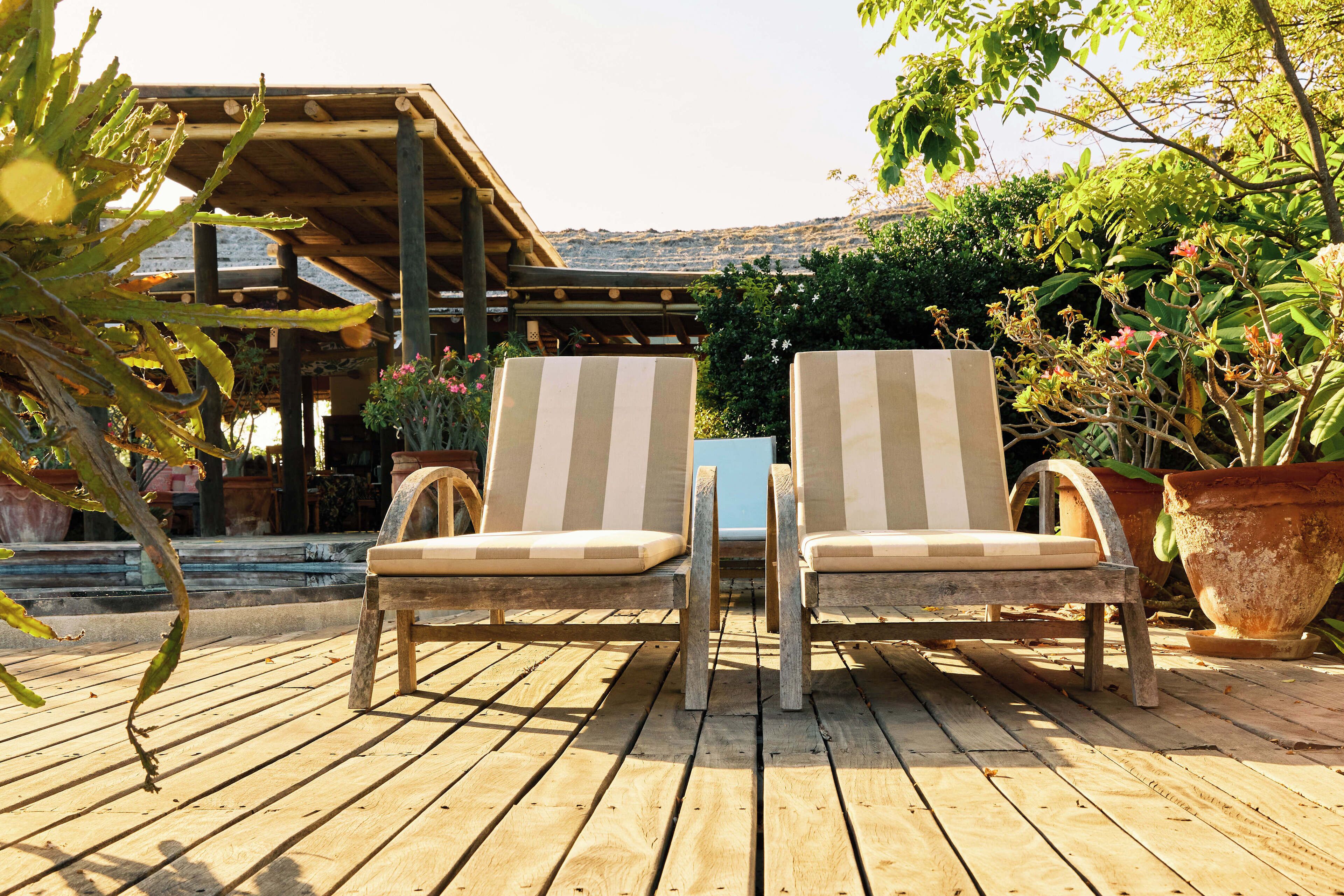 Deux fauteuils de jardin à rayures, placés sur une terrasse en bois, sous une pergola.