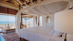 Une chambre avec un grand lit, un plancher en bois, une vue sur la mer et un balcon aménagé avec du mobilier d’extérieur.