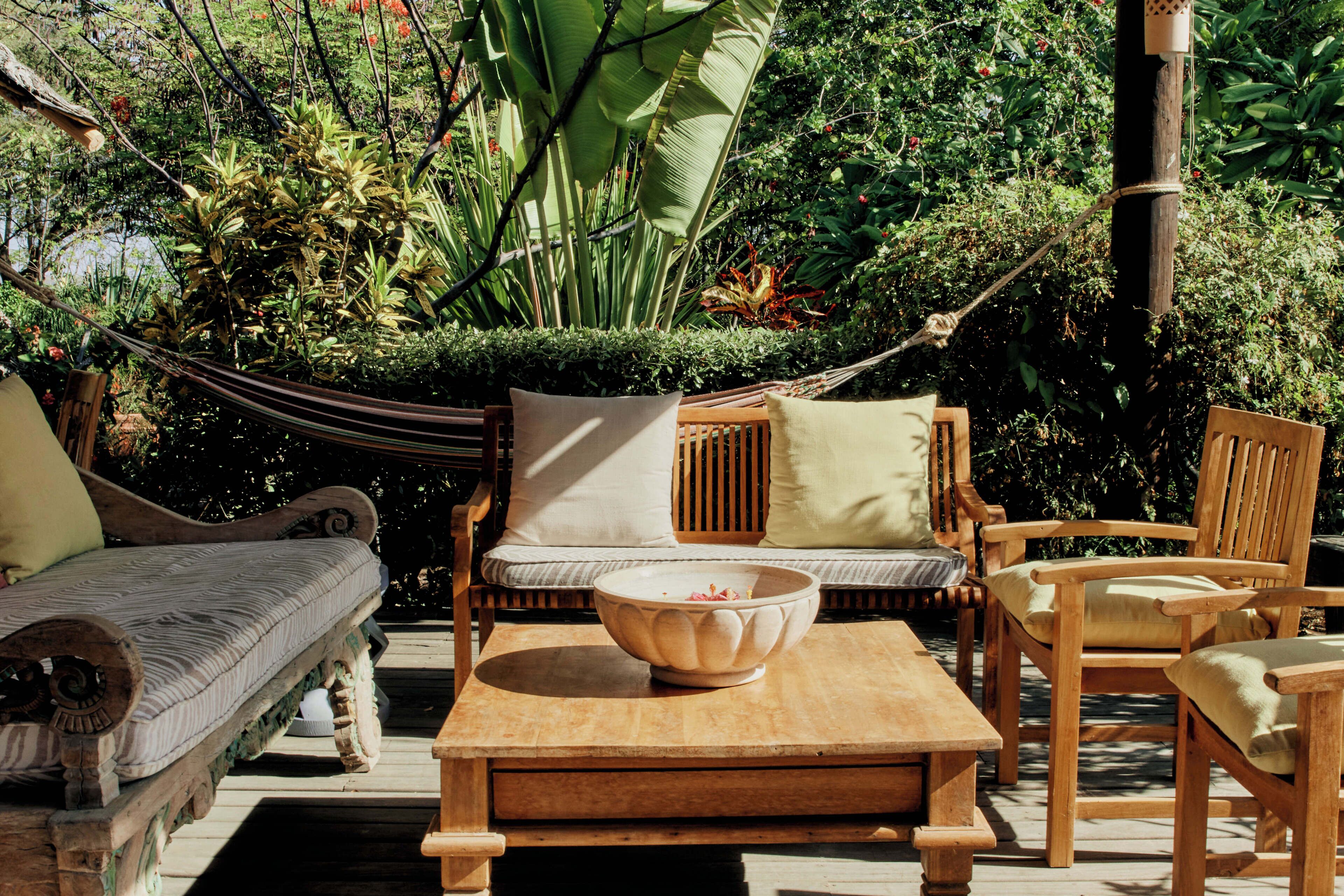 A wooden outdoor seating area with a hammock, cushioned chairs, and a table.