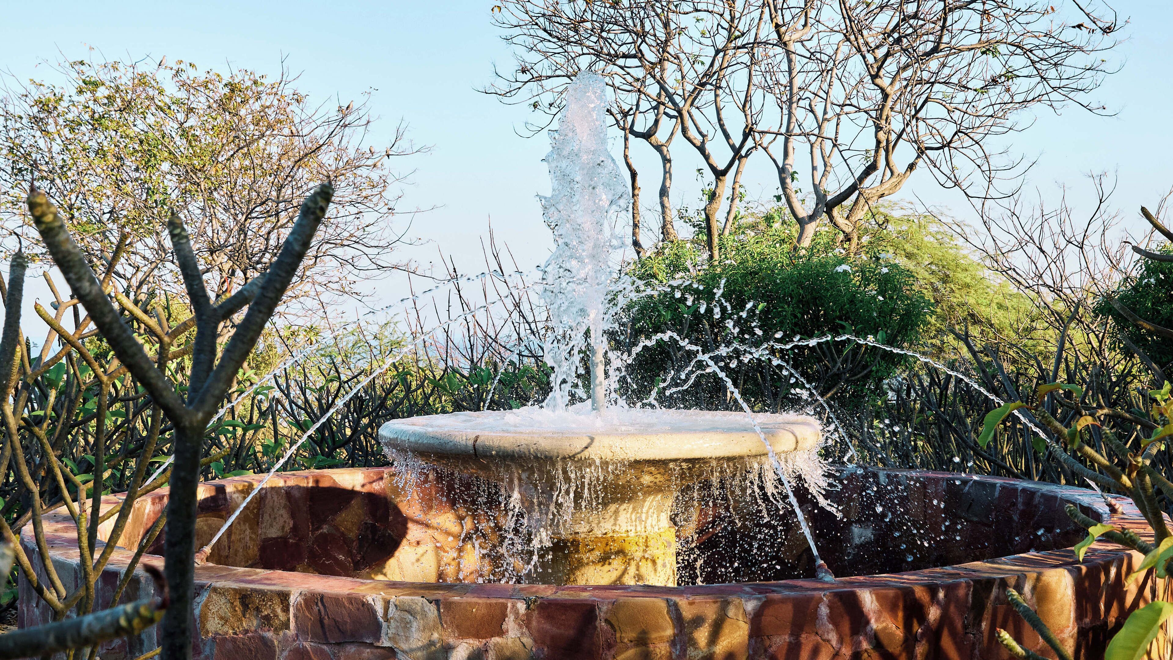 Une fontaine dont l’eau jaillit du centre, entourée de murs de pierre et de verdure.