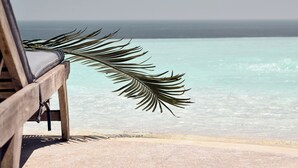 Un banc en bois orné de motifs de feuilles de palmier, donnant sur une plage aux eaux turquoise et cristallines.