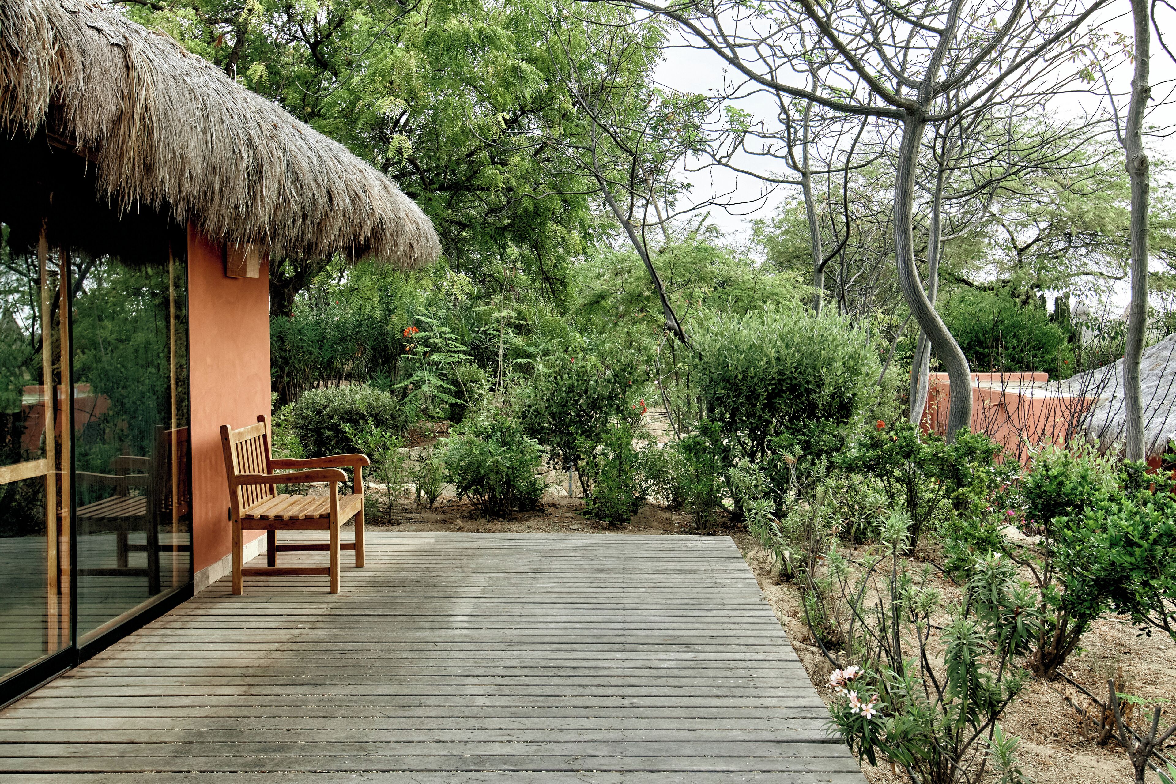 A wooden deck with a bench, a thatched-roof structure, and dense greenery.