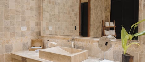 A bathroom with a beige tiled wall, a rectangular sink, a mirror, and a potted plant.