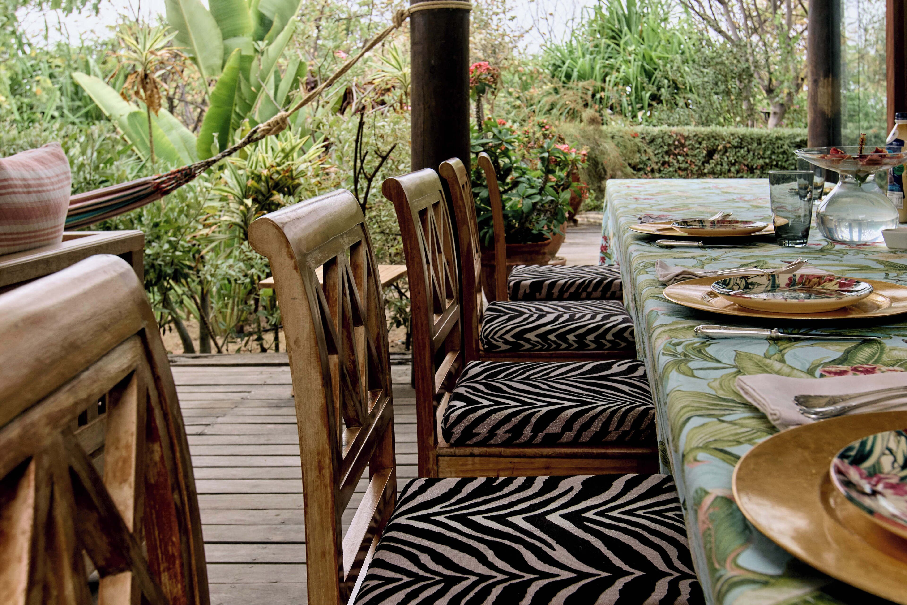 A wooden deck with a zebra-striped bench and a table set for dining, surrounded by lush greenery.