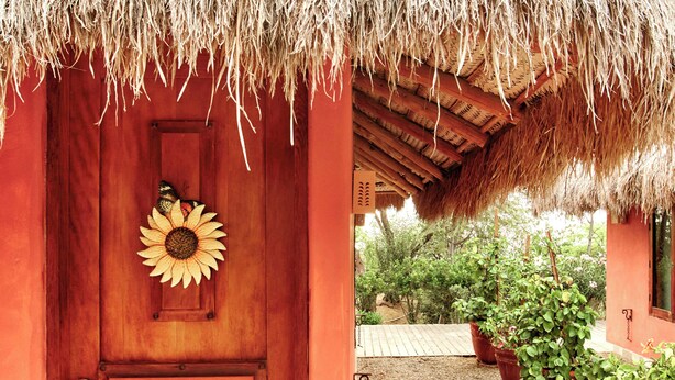 A wooden door with a sunflower decoration, a thatched roof, and potted plants in a garden area. - Villa Romana Boutique Hotel (Canoas de Punta Sal)