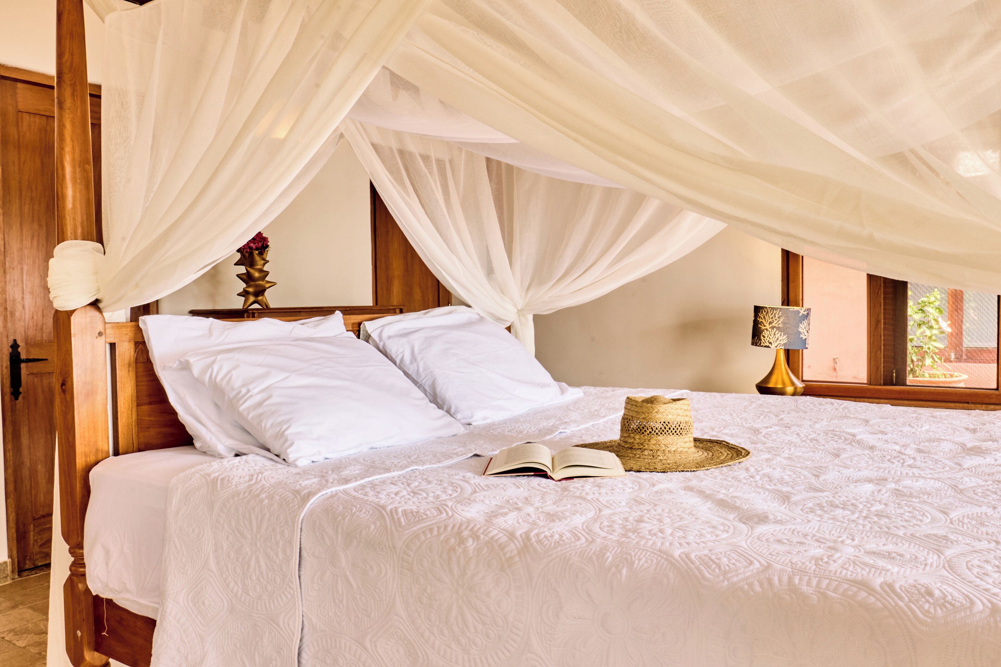 A bed with white linens, a straw hat, and an open book.