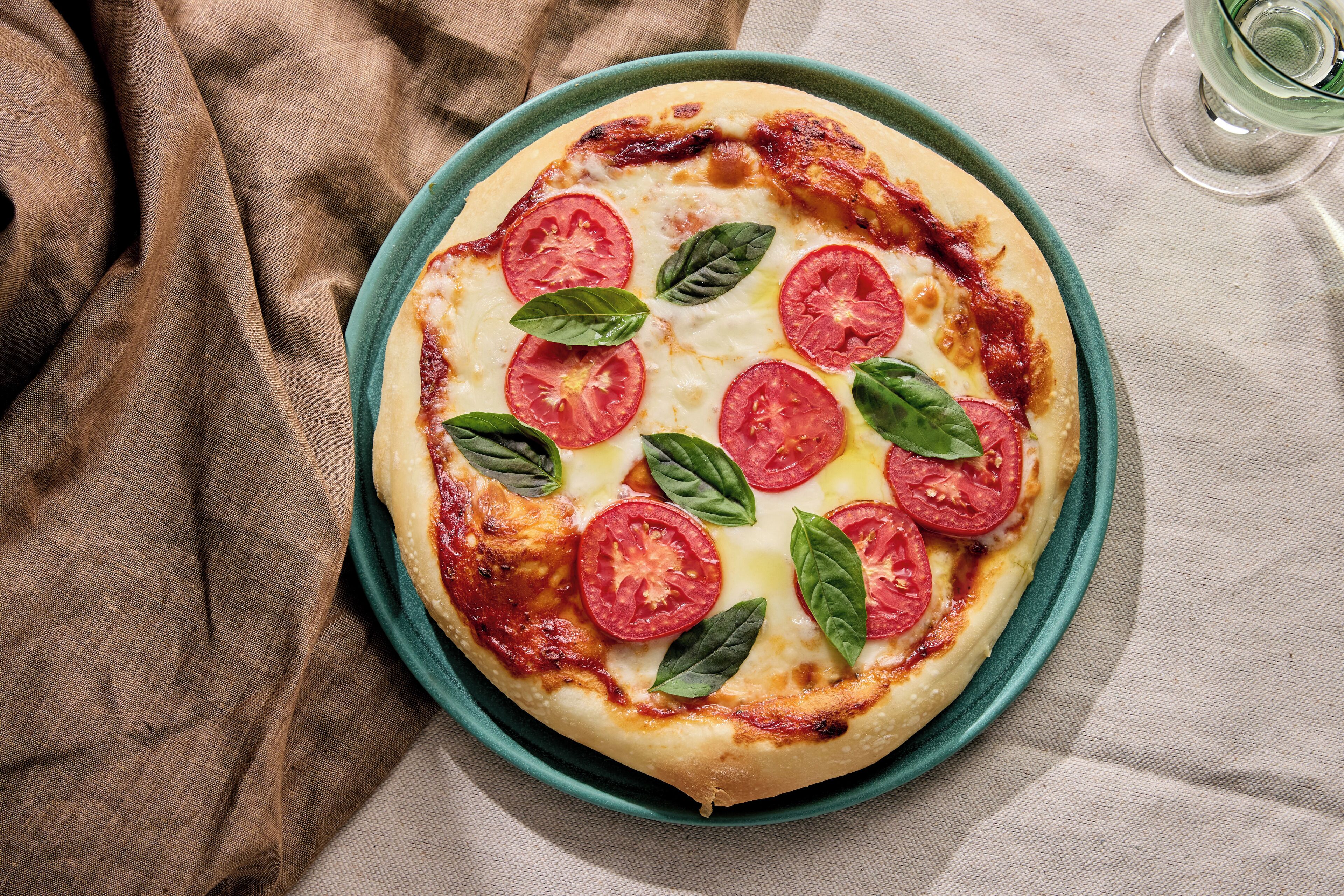 Una pizza con tomates y albahaca sobre un plato.