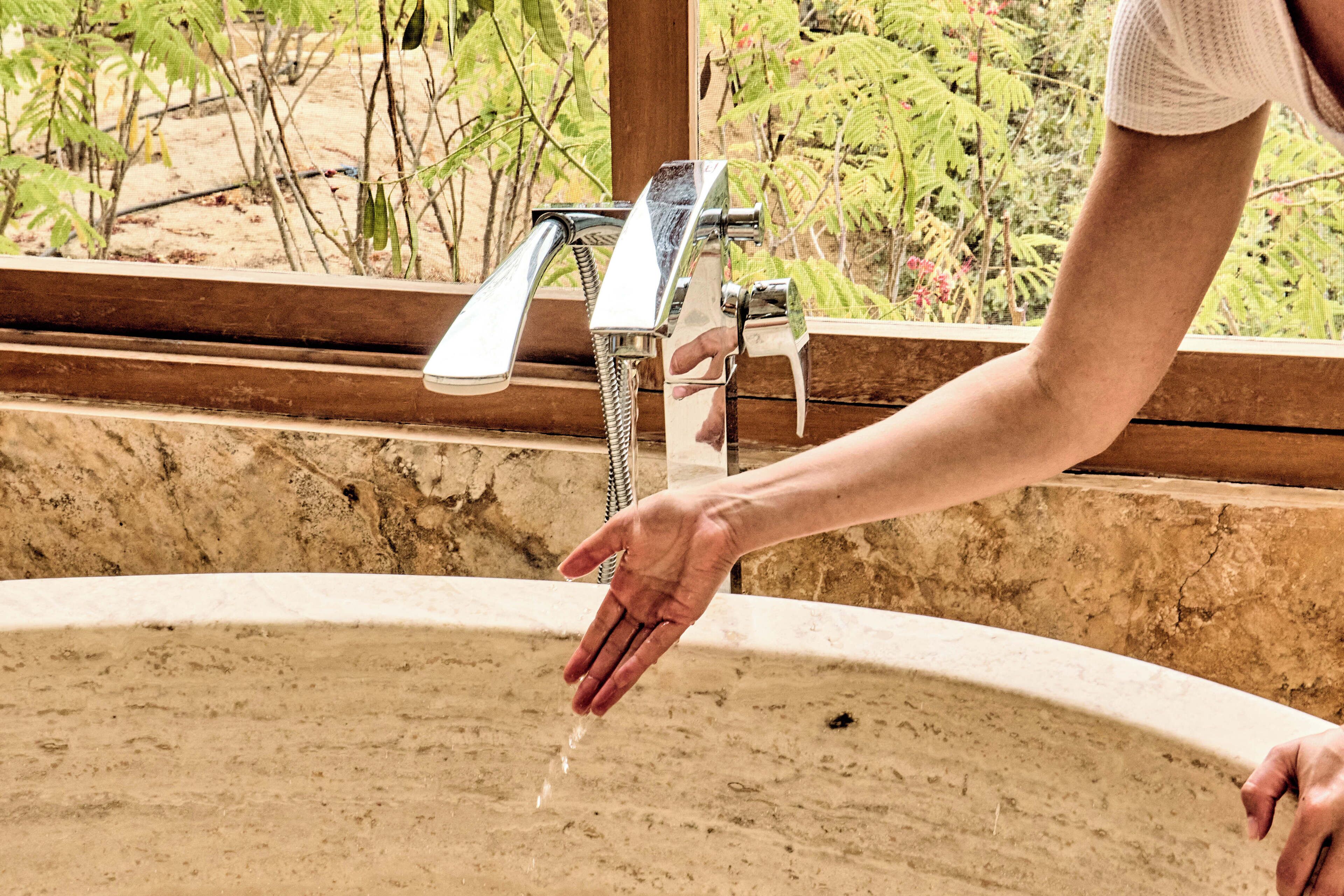 Una mano alcanzando agua de un grifo sobre un lavabo.