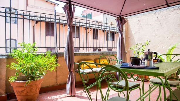 A patio with a table and chairs, a potted plant, and a view of buildings in the background.