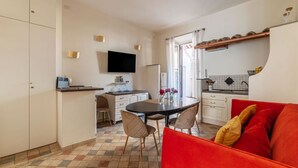 Une cuisine compacte avec un coin repas, un téléviseur fixé au-dessus du comptoir et un canapé rouge dans l’espace salon.