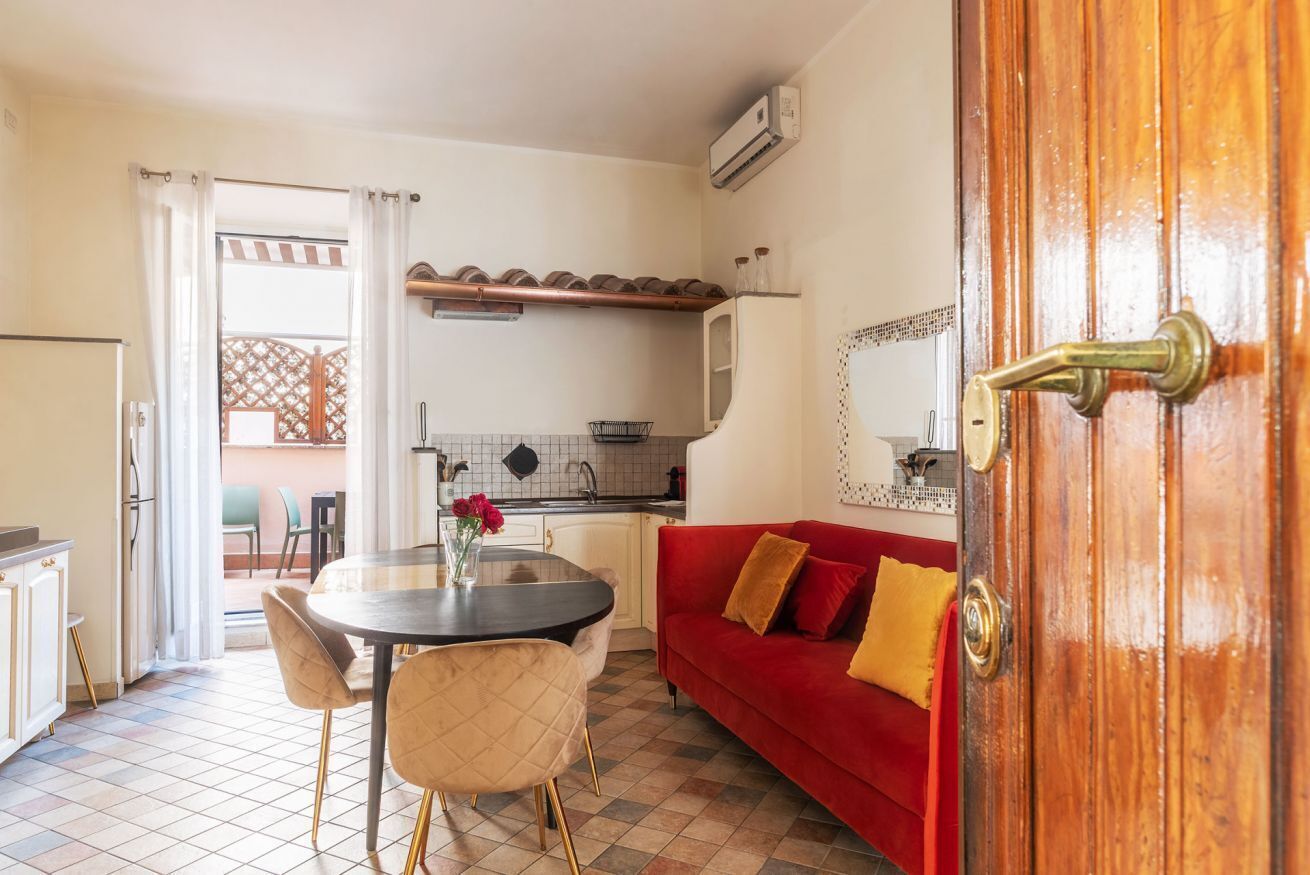 A compact kitchen with a dining area, a red sofa, and a wooden door.