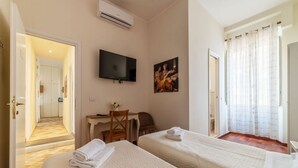 Une chambre d’hôtel avec deux lits, un bureau, une chaise, une télévision et un tableau au mur.