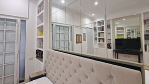 A bedroom with a large mirror, a tufted headboard, and built-in shelving with books and decorative items. - The Mirror Suite - Spanish Steps (Roma)