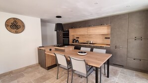 A modern kitchen with wooden cabinetry, a central island, and a dining area with chairs. - La Grange, in the heart of Périgord Noir, calm, serene and independent  (DAGLAN)