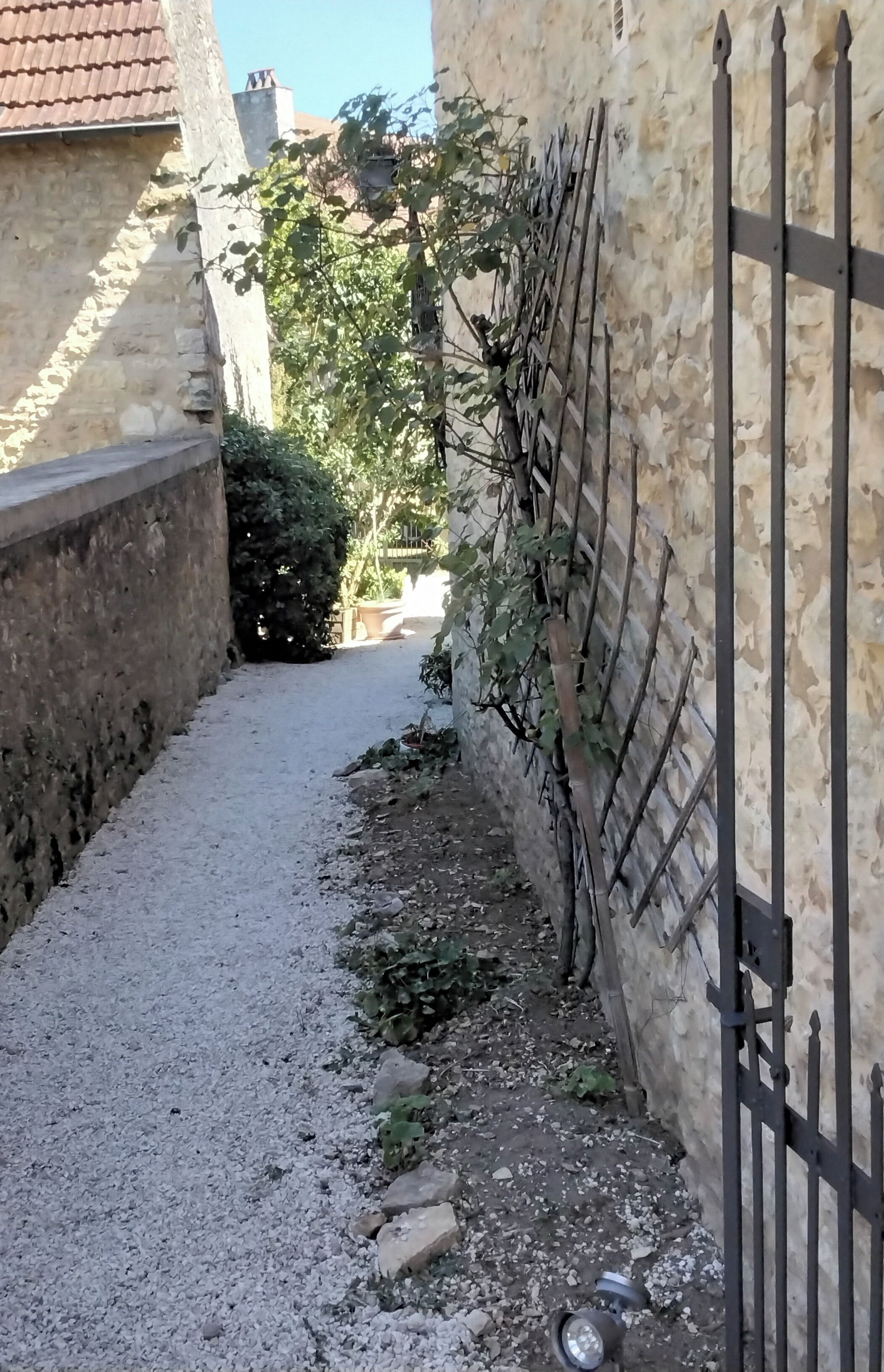A narrow alleyway with a gravel path, a stone wall on the left, and a metal fence on the right.