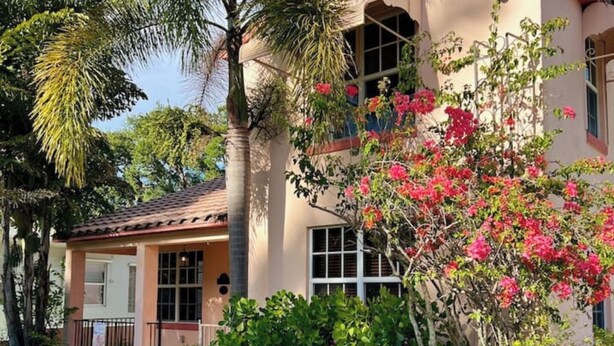 Una casa de dos pisos con techo de tejas, ventanas amplias y un jardín cuidado con diversas plantas y flores.
