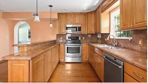 Una cocina con gabinetes de madera, electrodomésticos de acero inoxidable, encimeras de granito y lavavajillas integrado.