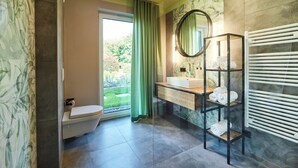 A bathroom with a toilet, sink, mirror, towel rack, and a view of greenery outside.