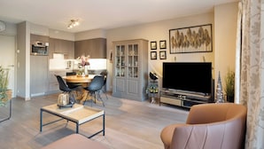 A modern living room with a sofa, a coffee table, a TV, and a dining area with chairs and a table. - Apartment in Blankenberge With Marina View (Blankenberge)