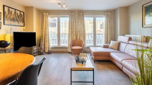 A modern living room with a sofa, a dining table, and a TV. - Apartment in Blankenberge With Marina View (Blankenberge)