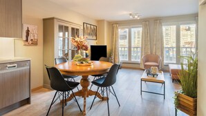 A modern living room with a wooden dining table, black chairs, a sofa, and a TV. - Apartment in Blankenberge With Marina View (Blankenberge)