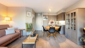 A modern living room with a sofa, coffee table, and dining area with chairs and a table. - Apartment in Blankenberge With Marina View (Blankenberge)
