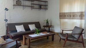 Un salon comprenant un canapé, des fauteuils, une table basse, un lampadaire, une bibliothèque et une plante en pot.