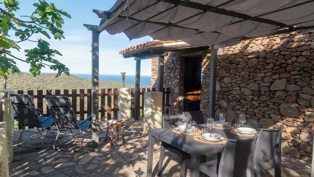 Une terrasse extérieure avec un mur en pierre, une table dressée pour le repas et des chaises longues.
