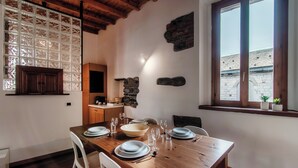A dining area with a wooden table set for four, white chairs, and a stone wall with a window above. - Loft Madera (Como)