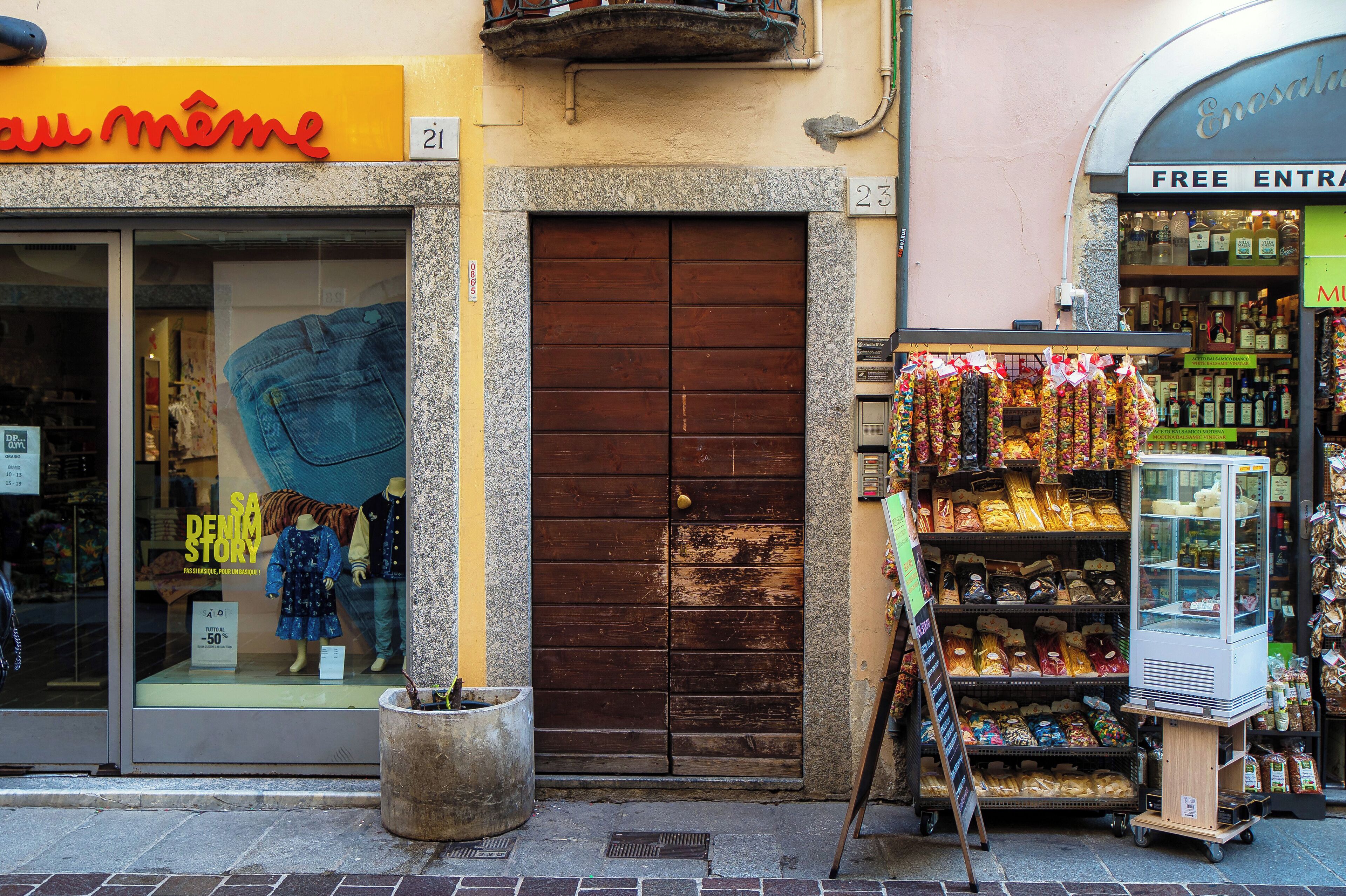 A storefront with a large wooden door, a mannequin in the window, and a display of snacks outside.