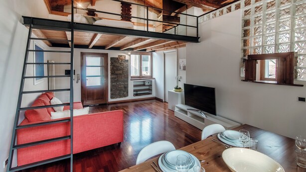 A loft-style room with a wooden ceiling, a red sofa, a dining table set with plates and glasses, and a TV in the corner. - Loft Madera (Como)