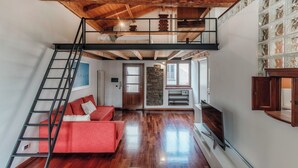 A loft-style room with a wooden ceiling, a red sofa, a TV, and a stone wall. - Loft Madera (Como)