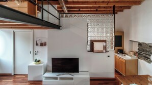 A modern living room with a wooden ceiling, a flat-screen TV on a white stand, a stone fireplace, and a kitchen area with wooden cabinets. - Loft Madera (Como)