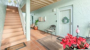 Una escalera que conduce a un rellano con una puerta, una silla y una planta en maceta.