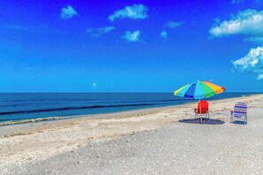 Een strand met een kleurrijke parasol en twee gestreepte strandstoelen.