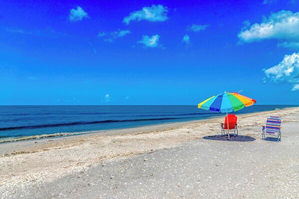 Una playa con un paraguas de colores y dos sillas de playa a rayas.