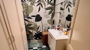 A bathroom with a checkered floor, a sink with toiletries, and a shower curtain with a leaf pattern. - Character apartment in Bordeaux - 78 m² - Saint-Seurin / Croix-Blanche (Bordeaux)